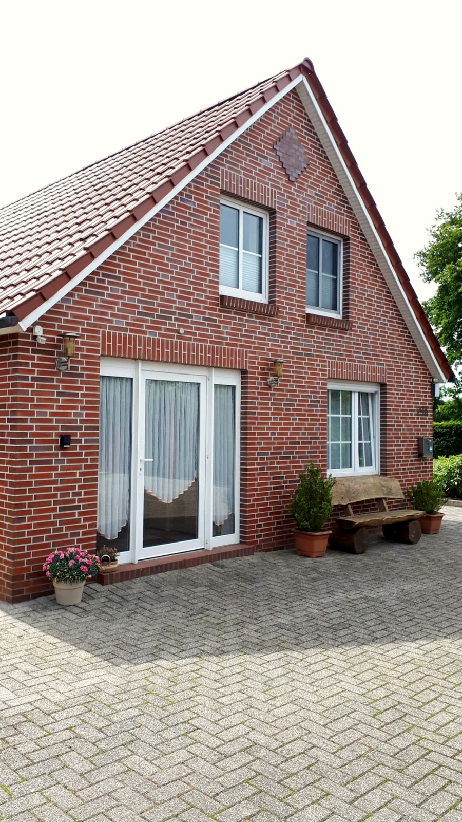 Haus Moorgrund von außen: rotes Klinkerhaus mit Giebel, Eingang zur Wohnung im Erdgeschoss, Sitzbank und gepflasterter Hof