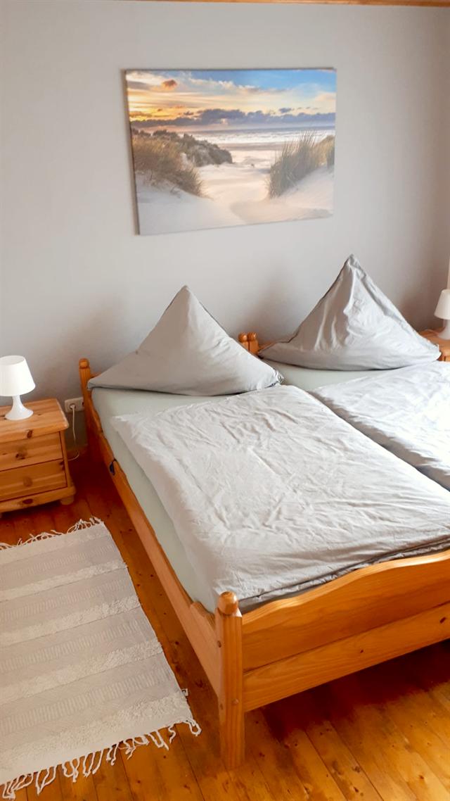 Schlafzimmer mit zwei Einzelbetten aus Holz, Nachttischen und Dielenboden